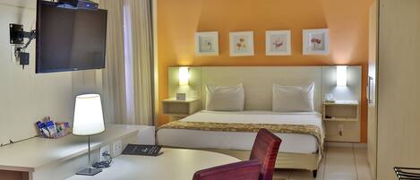 Una habitación de hotel con una cama, mesitas de noche, un escritorio con lámpara, una silla y un televisor fijado a la pared.