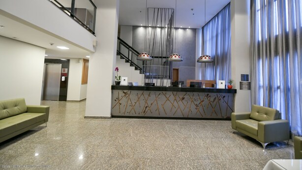 A modern lobby with a reception desk, two sofas, a staircase, and a large window with curtains.