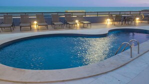 A swimming pool with lounge chairs and tables, a tiled deck, and a view of the ocean. - Reymar Hotel Maceió (Maceió)