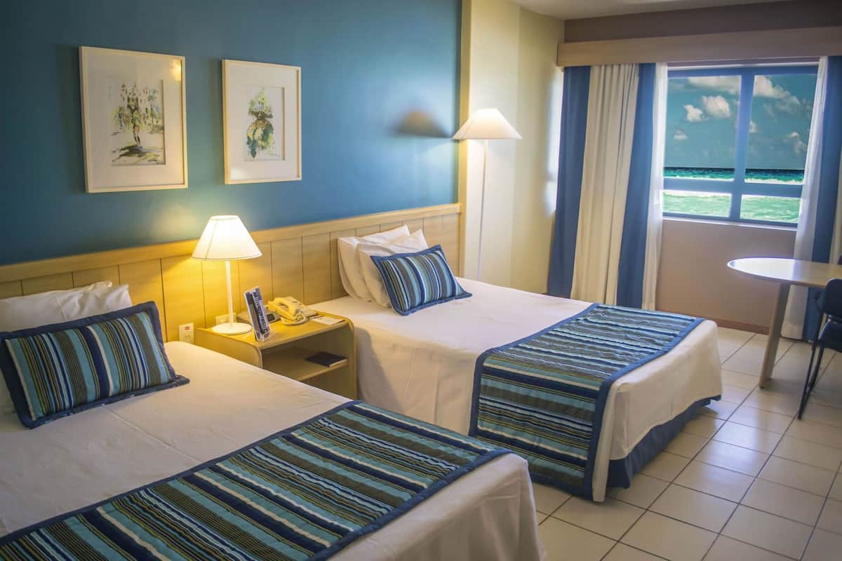 A hotel room with two beds, a nightstand with a lamp, a telephone, and a window with curtains.