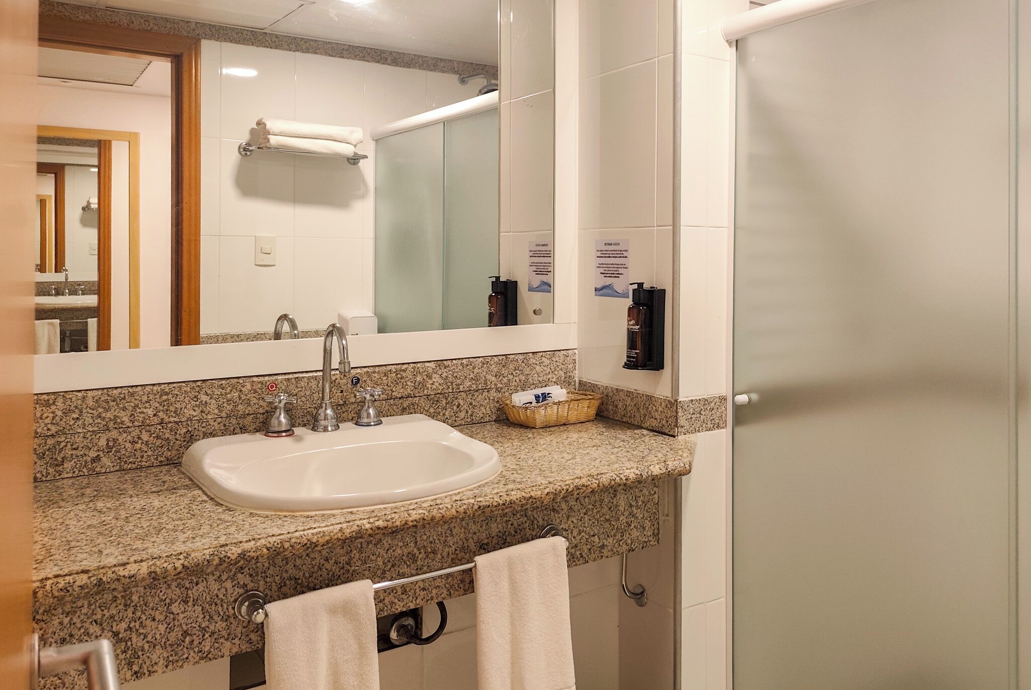 A bathroom with a granite countertop sink, a mirror, a towel rack, and a glass shower enclosure.