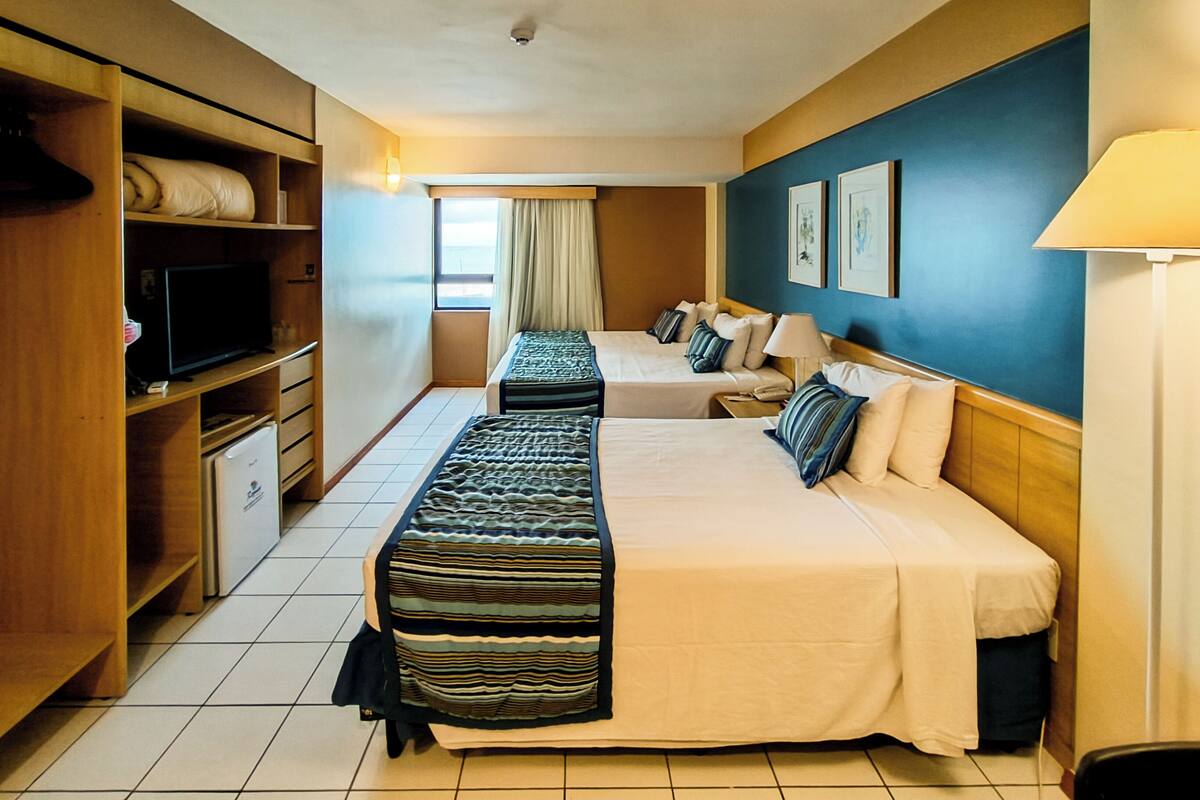 A hotel room with two beds, a television, a wardrobe, and a window with curtains.