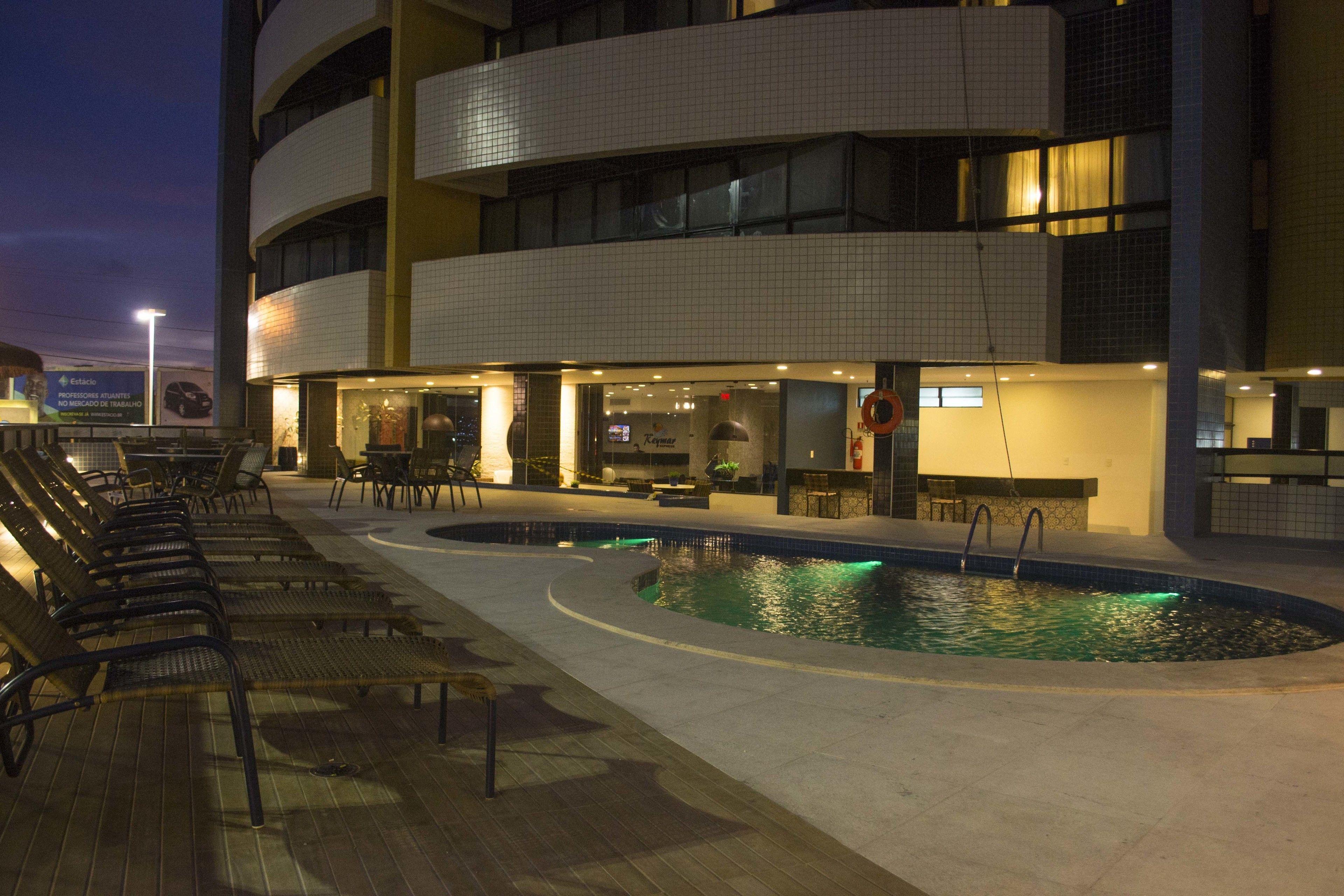 A pool area with lounge chairs and a restaurant.