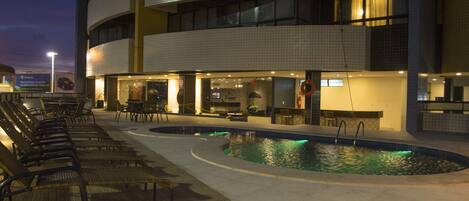 A pool area with lounge chairs and a restaurant.