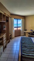 Habitación de hotel con cama, escritorio, silla, armario y ventana con vista a la playa.
