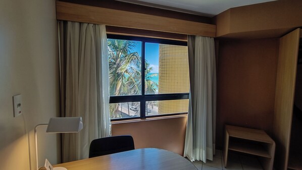A hotel room with a large window, a desk, a chair, and a small table.