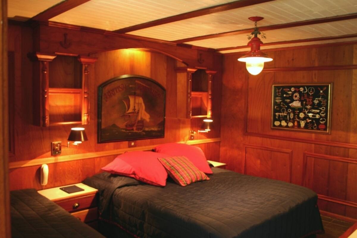 Una habitación con paneles de madera, una cama, una mesita de noche, una lámpara y un cuadro en la pared.