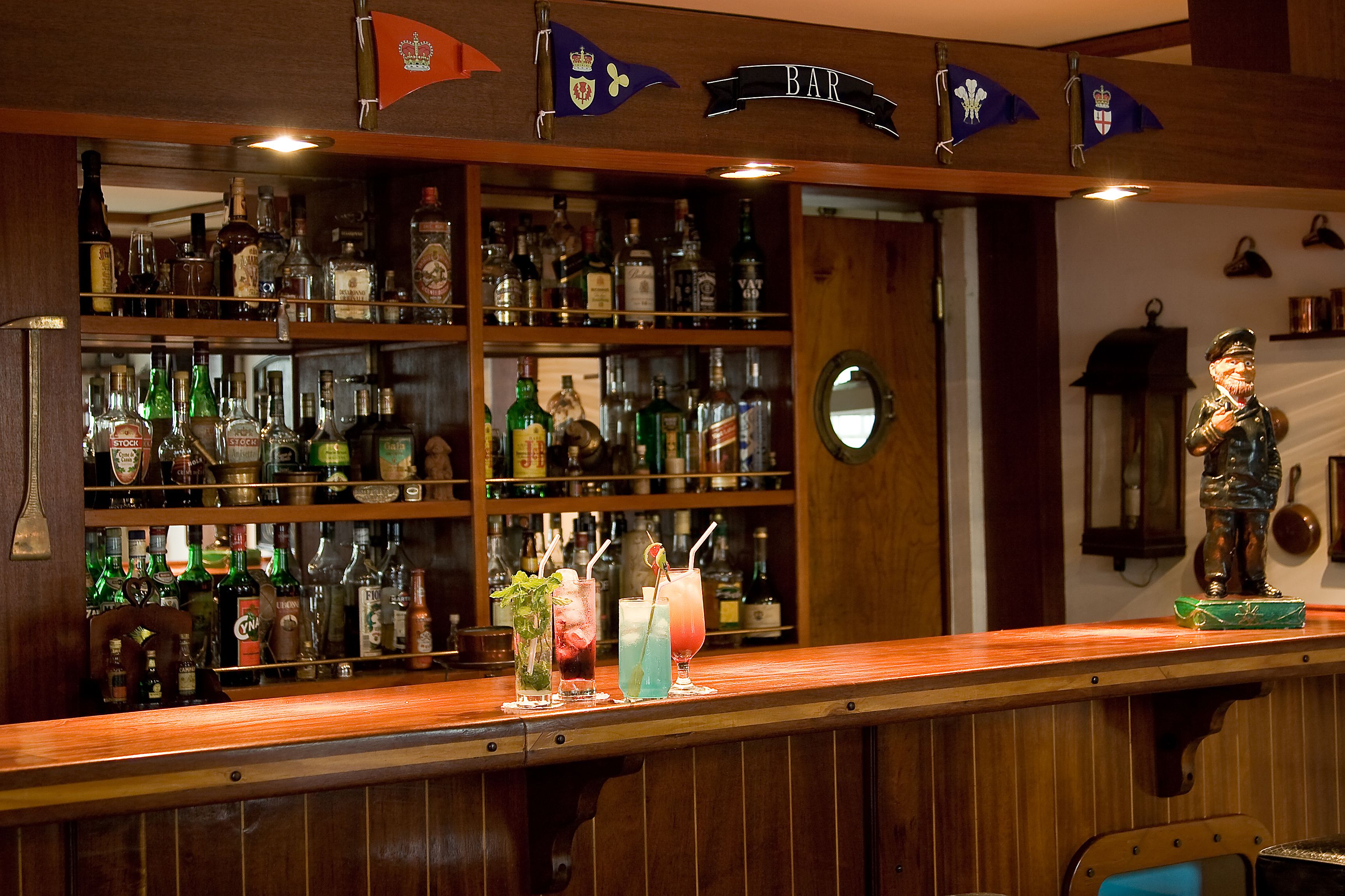 A bar area with shelves of various liquor bottles, a counter with drinks, and a statue.