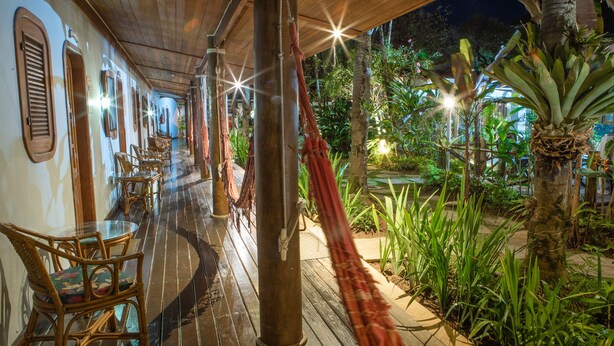 A covered outdoor area with wooden flooring, wicker furniture, and a hammock.