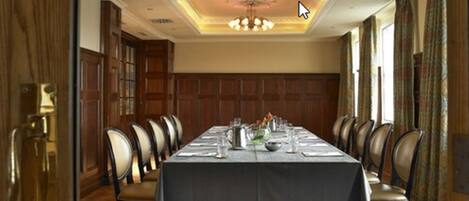 Un comedor formal con una larga mesa dispuesta para una comida, paneles de madera en las paredes y un candelabro.