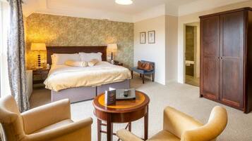 A hotel room with a bed, bedside tables, a desk, two armchairs, a wardrobe, and a carpeted floor.