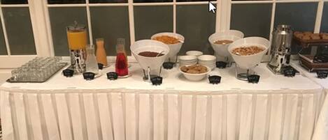 Un tavolo da buffet con diversi cibi e bevande, sullo sfondo una finestra con persiane.