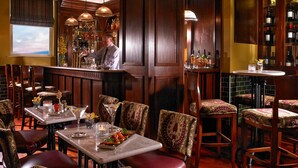 Zona de bar con paneles de madera, un barman y una exhibición de vinos.