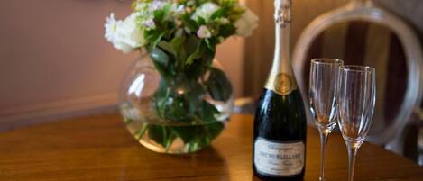 A table with a bottle of champagne, two glasses, a plate of strawberries, and a vase of flowers.