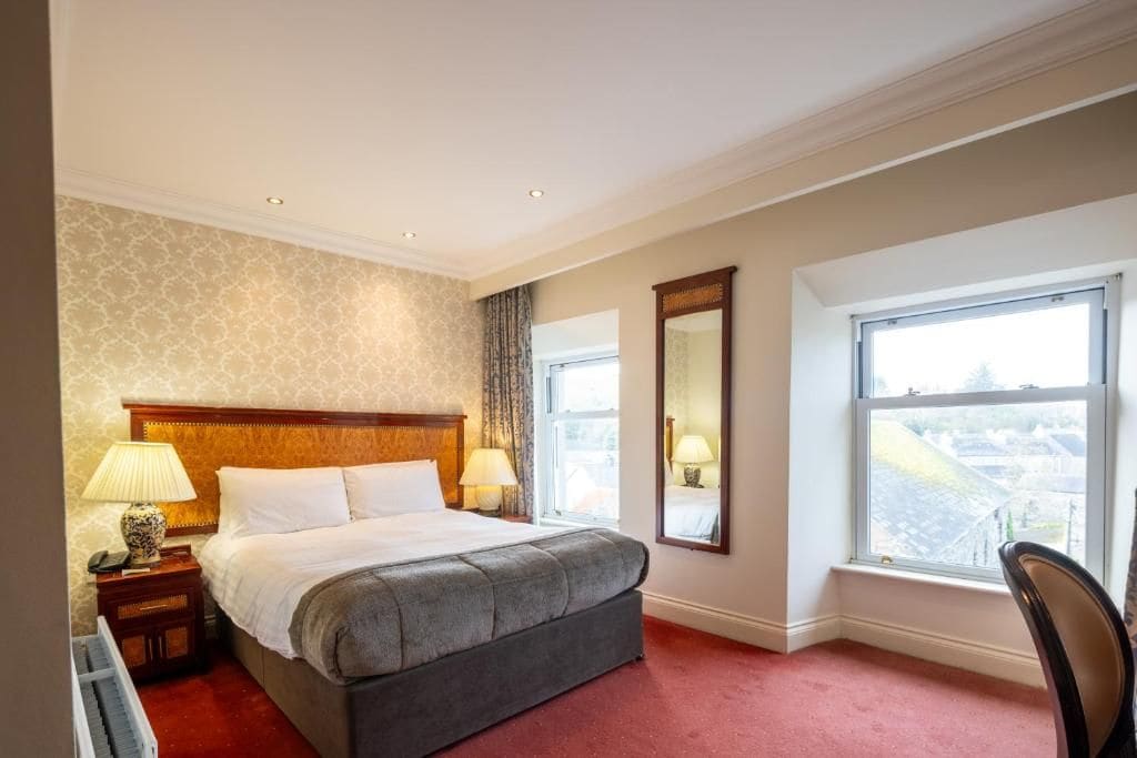 Una habitación de hotel con una cama grande, dos lámparas de noche, un espejo y una ventana con vistas.