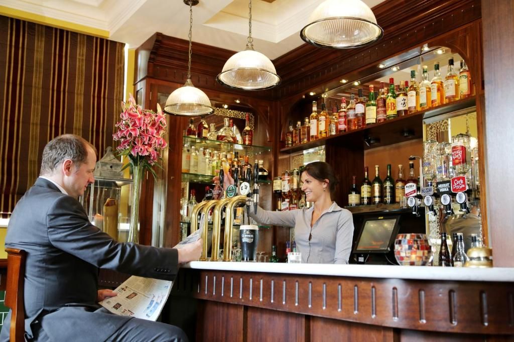A bar area with a bartender serving a customer. There are multiple taps and bottles on the shelves.