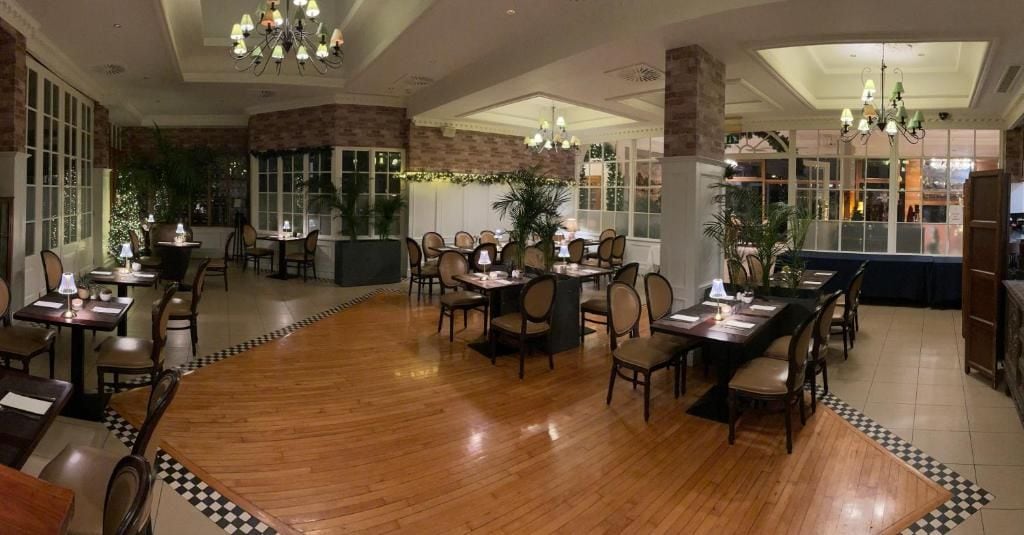 A spacious dining area with multiple tables and chairs, a wooden floor, and decorative lighting fixtures.