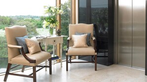 A modern interior with two leather armchairs, a white table with a vase, and a large window offering a view of greenery.