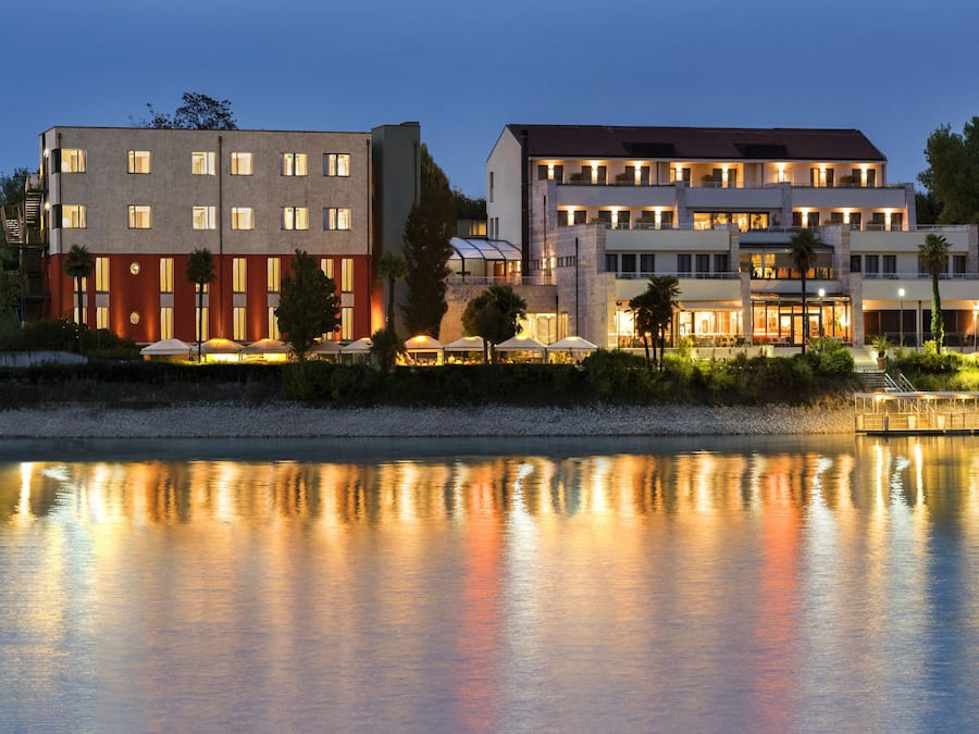 A hotel with multiple buildings, a reflective water body in front, and outdoor seating areas.