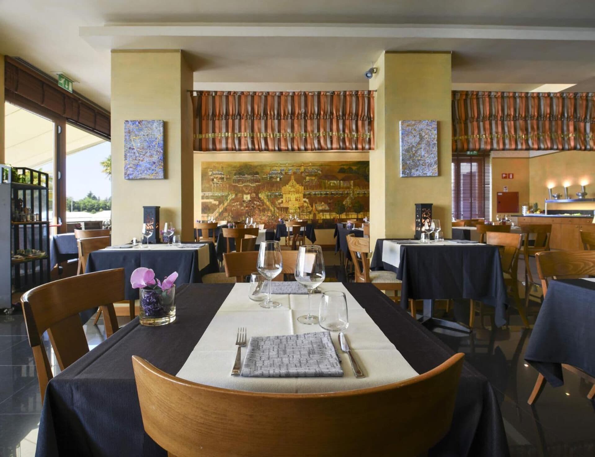A restaurant with tables set for dining, featuring artwork on the walls and a view of the cityscape.