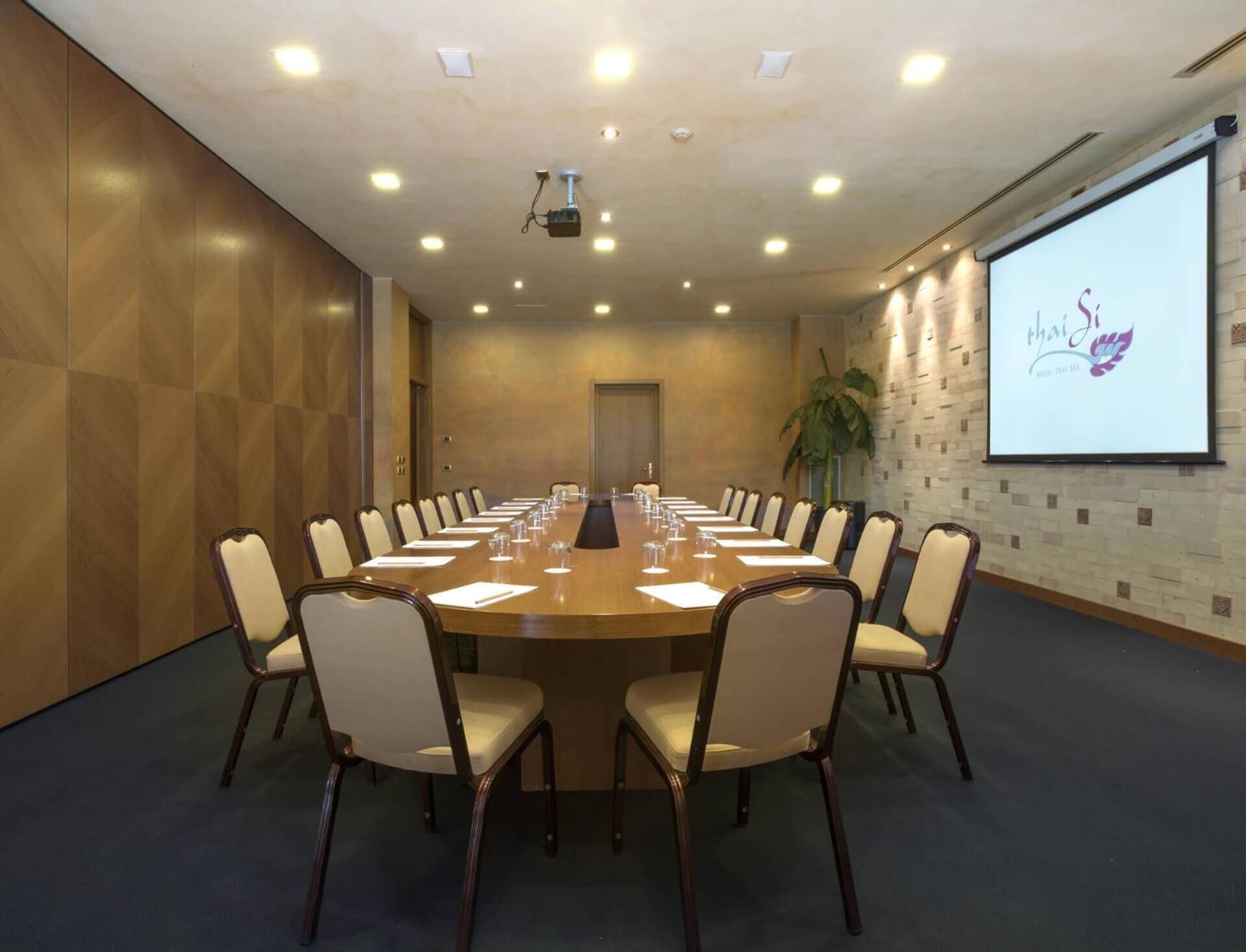 A conference room with a long table, chairs, and a projector screen displaying a logo.