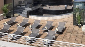 Un espace piscine aménagé sur le toit, avec des chaises longues et un mur en pierre.
