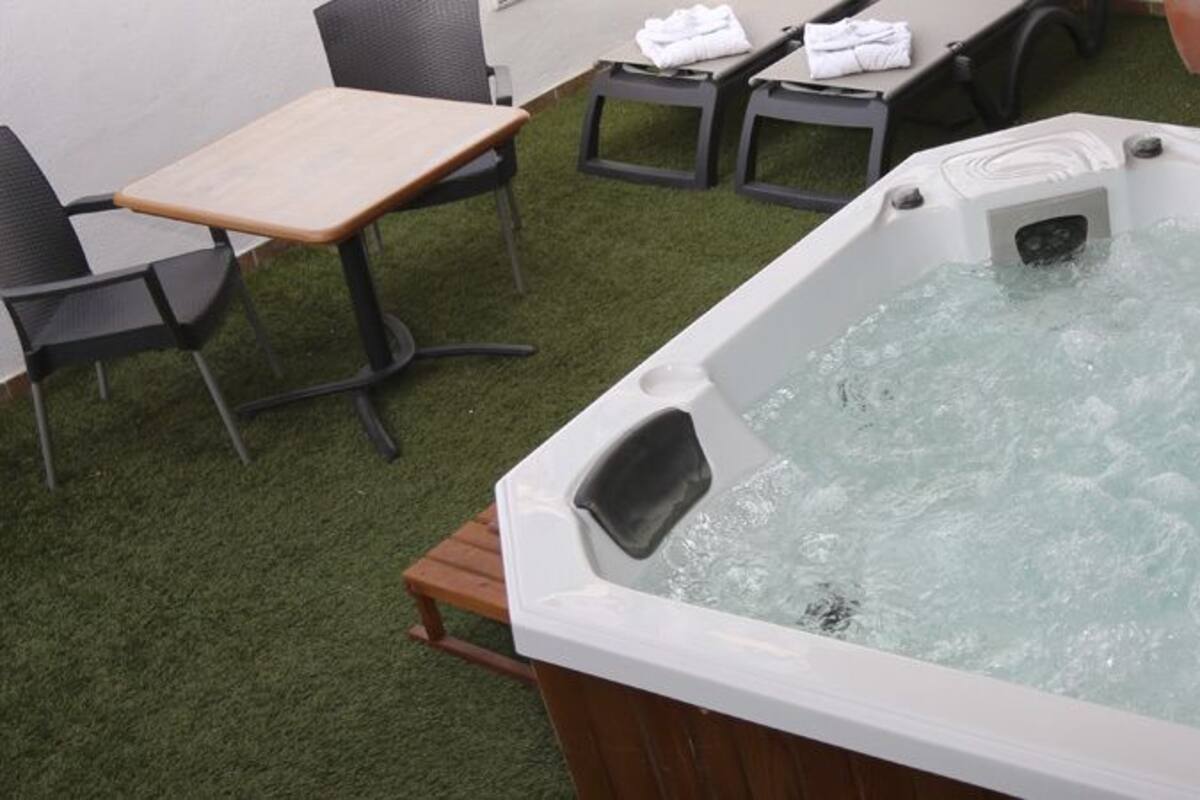 Un bain à remous avec une table et des chaises en bois, entouré de gazon synthétique.