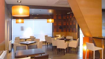 A modern dining area with tables and chairs, large pendant lights, and a patterned wall.