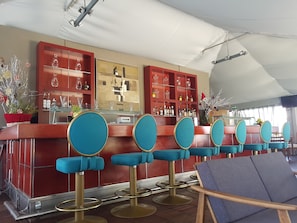 Un espace bar doté de plusieurs tabourets et d’un comptoir, d’un grand miroir et d’étagères remplies de bouteilles.