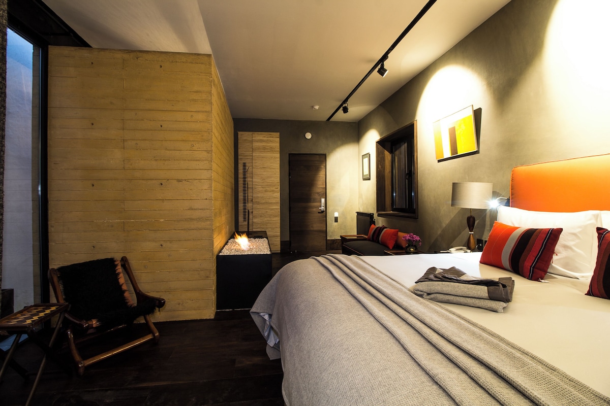 Une chambre d’hôtel avec un lit, une chaise, une petite table et un téléviseur fixé au mur.