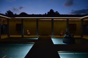 Un bâtiment moderne doté d’un espace extérieur couvert, d’une piscine et d’un coin salon avec une table et des chaises.