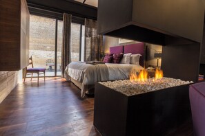 Ein modernes Schlafzimmer mit Bett, Nachttisch, Kamin und Blick ins Freie.