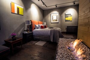 Une chambre moderne avec un lit, des tables de chevet, une commode, une cheminée et des œuvres d’art accrochées aux murs.