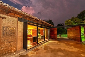 Un hôtel moderne doté d’une façade en pierre et de grandes portes vitrées donnant sur un espace extérieur aménagé pour se détendre.
