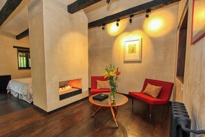 Une pièce chaleureuse avec une cheminée, un canapé rouge, une table ronde ornée d’un vase et un tableau encadré accroché au mur.