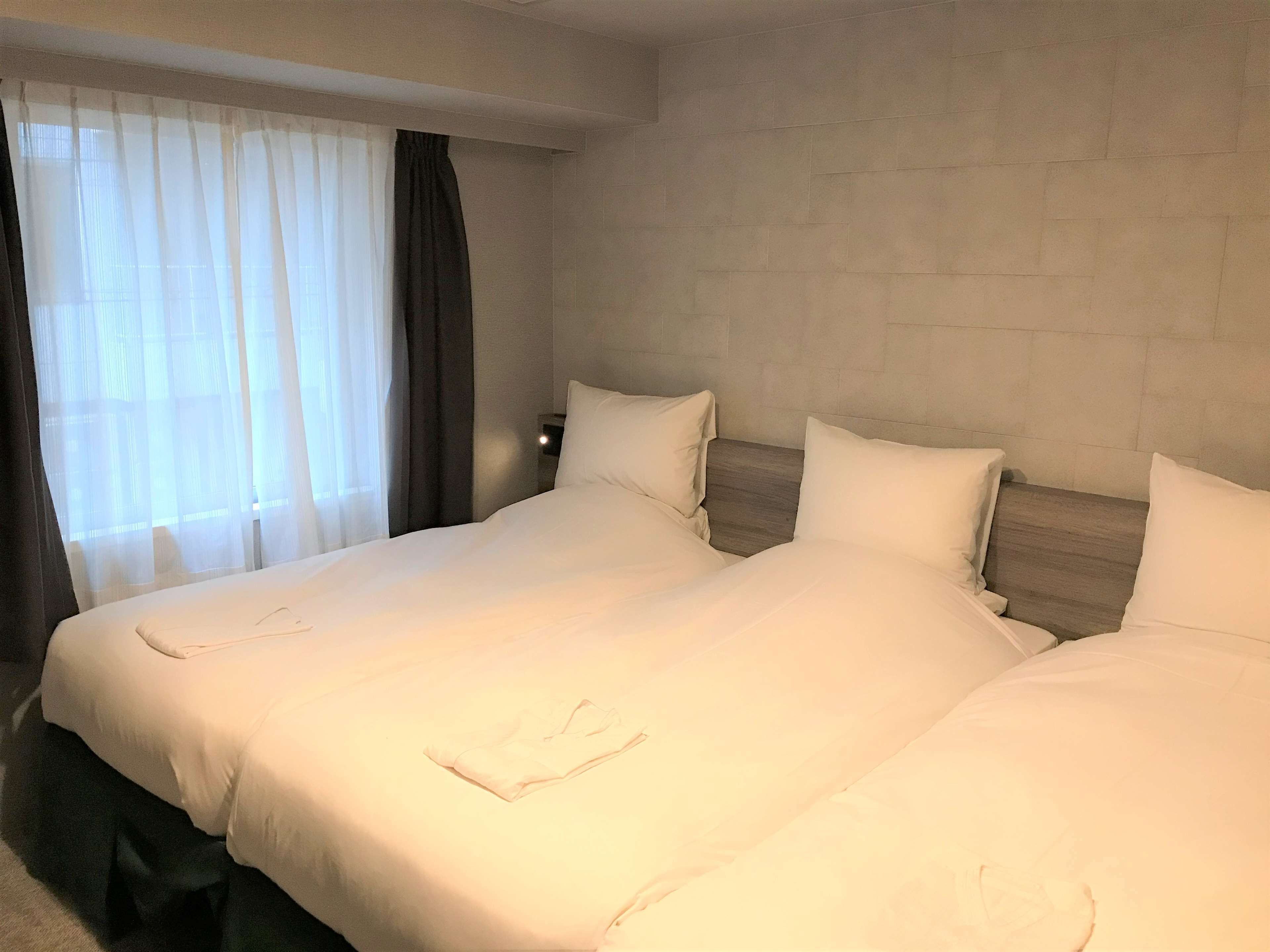 A hotel room with a large bed, a nightstand, and a window with sheer curtains.