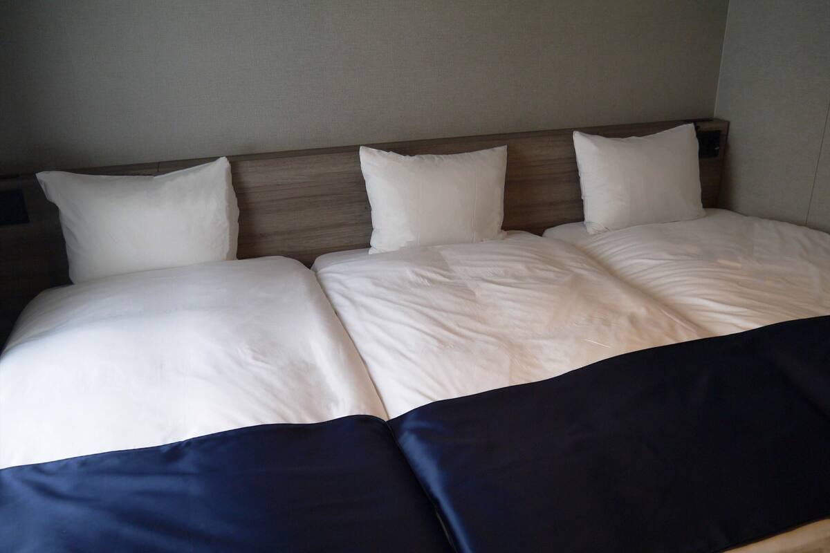 A bed with white and navy bedding, a wooden headboard, and a neutral wall.
