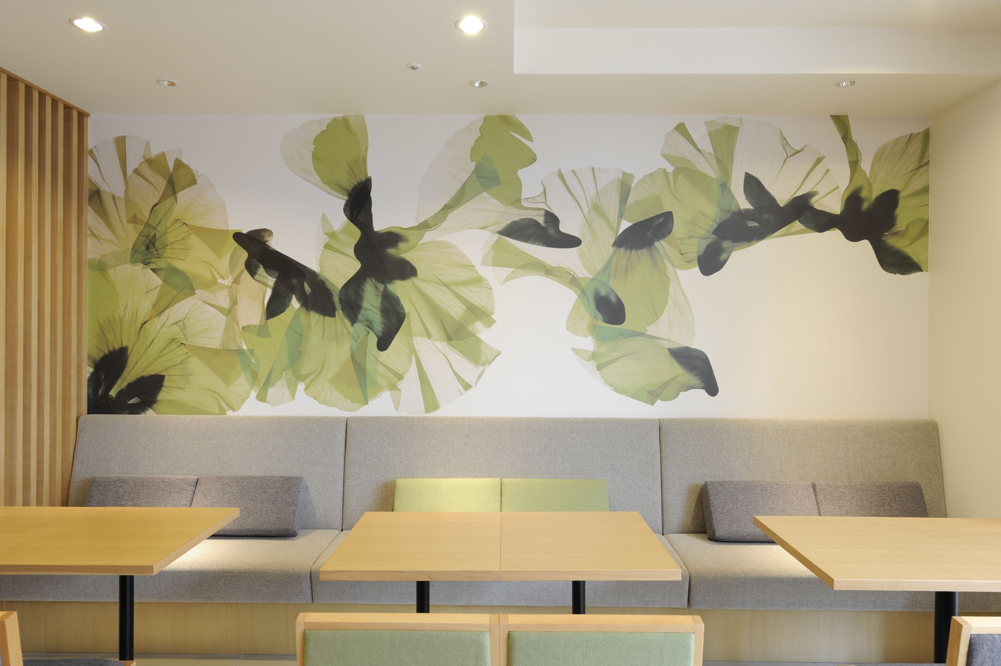 A modern interior with a sofa and tables, a wall mural with abstract leaf patterns, and recessed ceiling lighting.