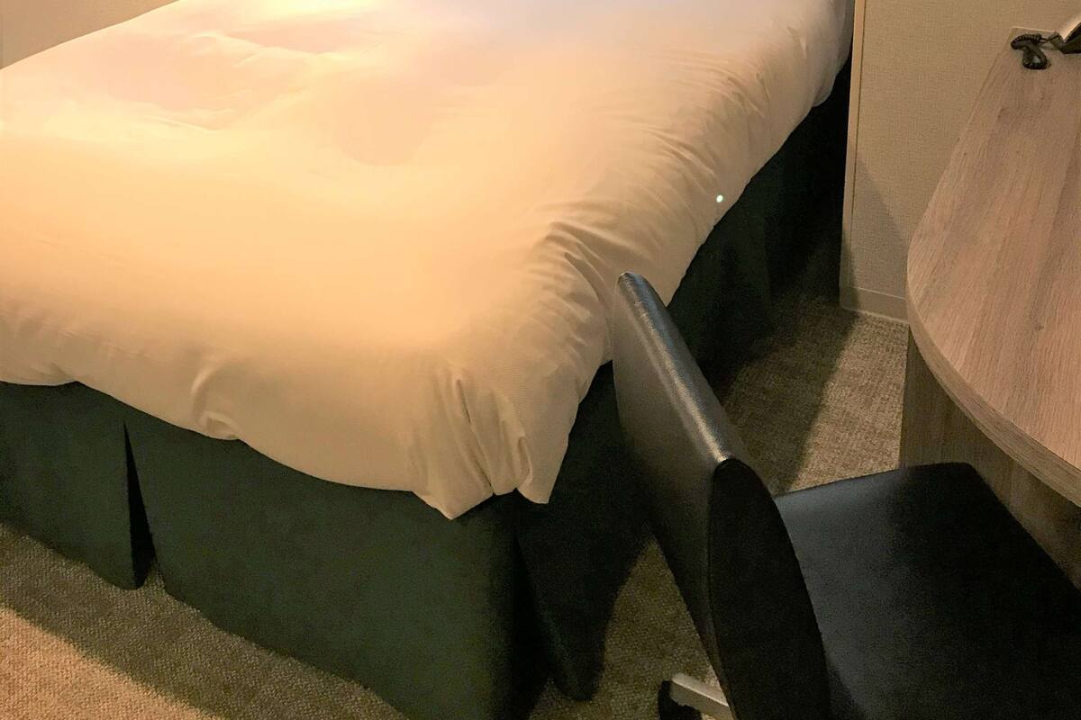 A neatly made bed with white linens in a hotel room.
