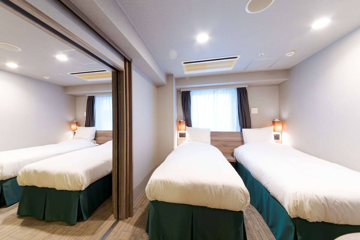A hotel room with two single beds, a large mirror, and a ceiling with recessed lighting.
