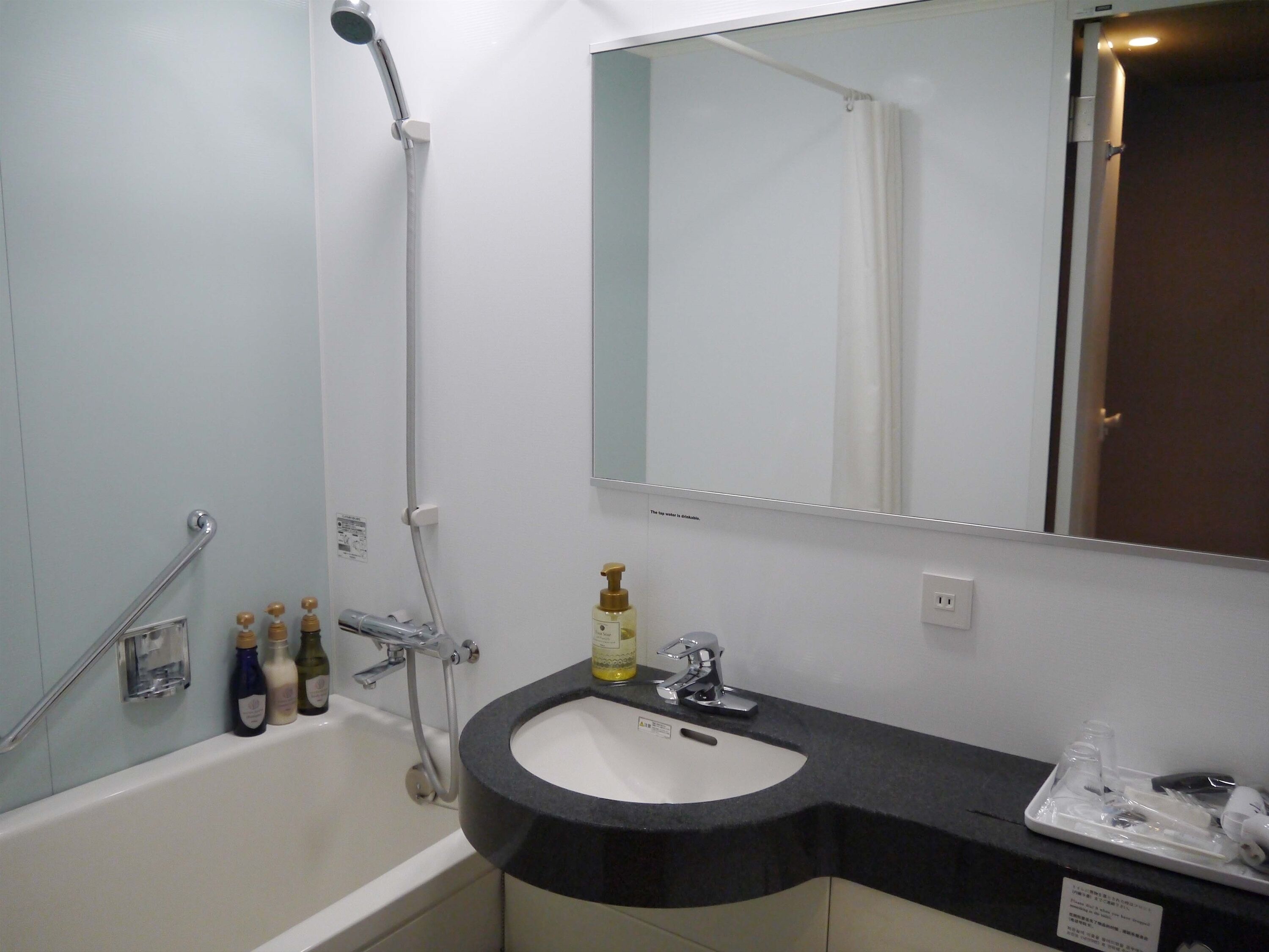 A bathroom with a bathtub, a sink, a mirror, and toiletries.