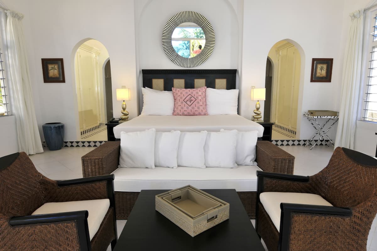 Una habitación de hotel con una cama grande, dos mesitas de noche, una mesa de centro y dos sillas de mimbre.