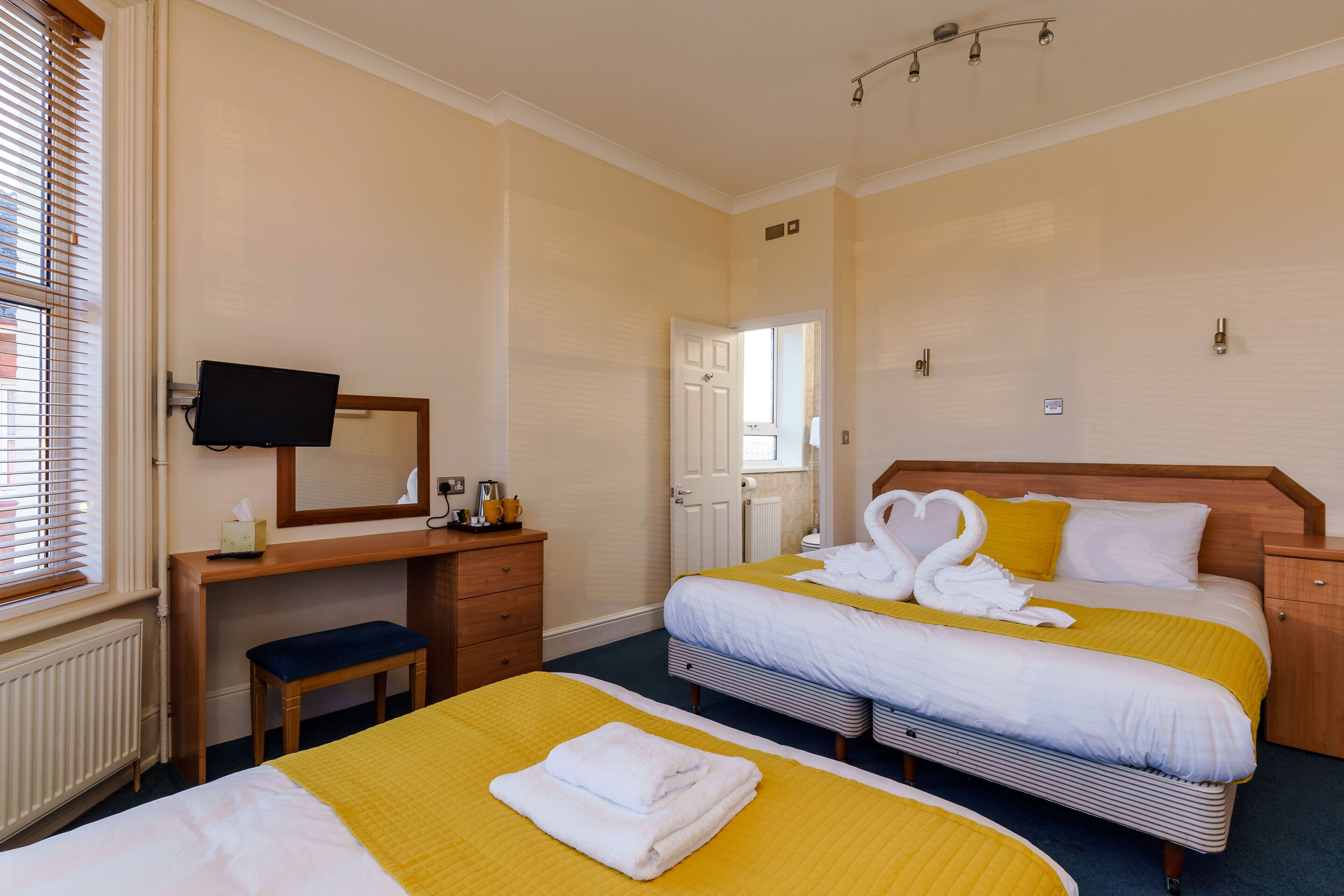 Habitación de hotel con dos camas, un escritorio con televisor y una ventana con persianas.