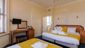 Habitación de hotel con dos camas, un escritorio con televisor y una ventana con persianas.