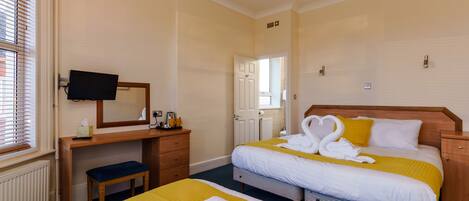 A hotel room with two beds, a desk with a television, and a window with blinds.