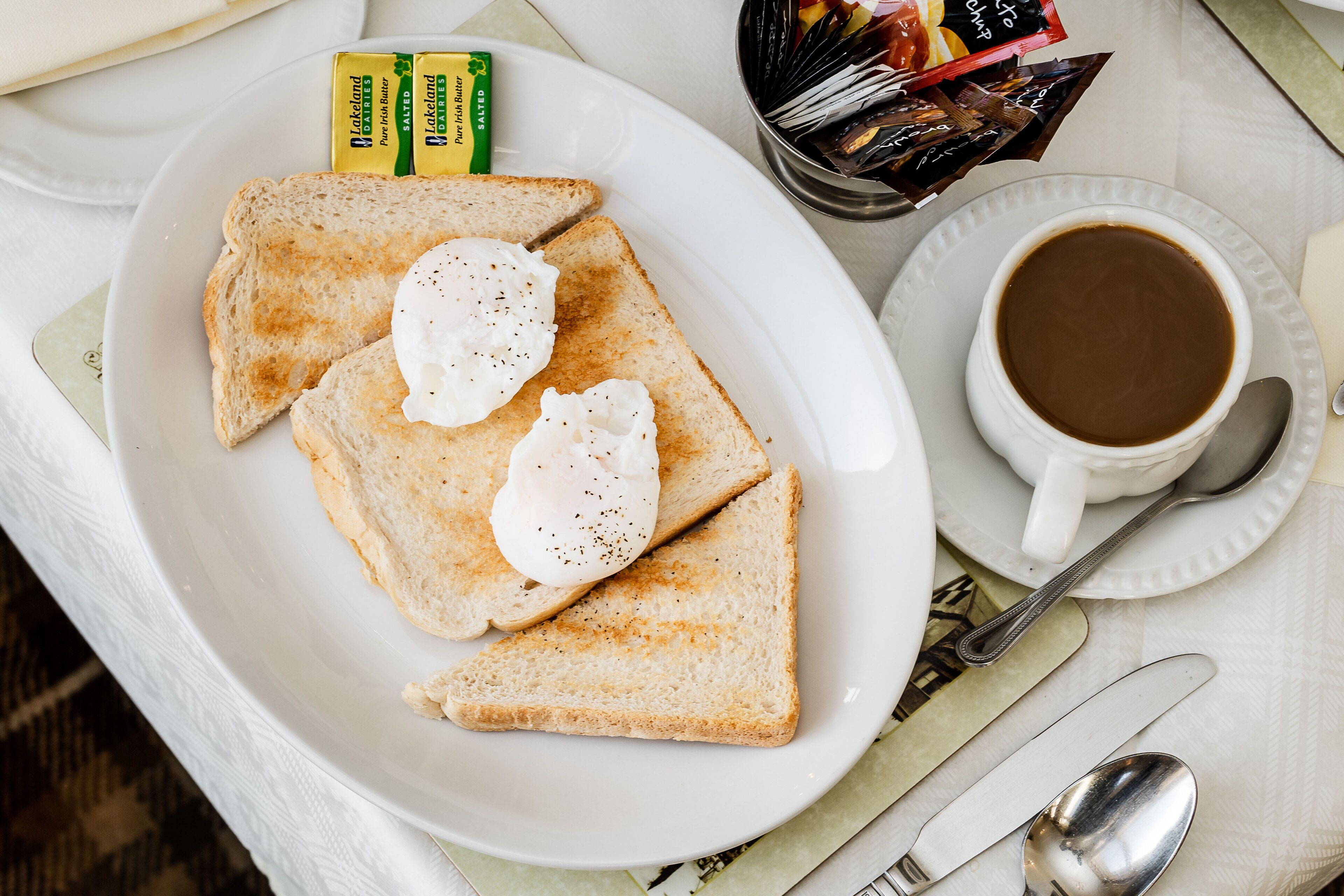 A breakfast plate with toast and poached eggs, a cup of coffee, and condiments on a table.