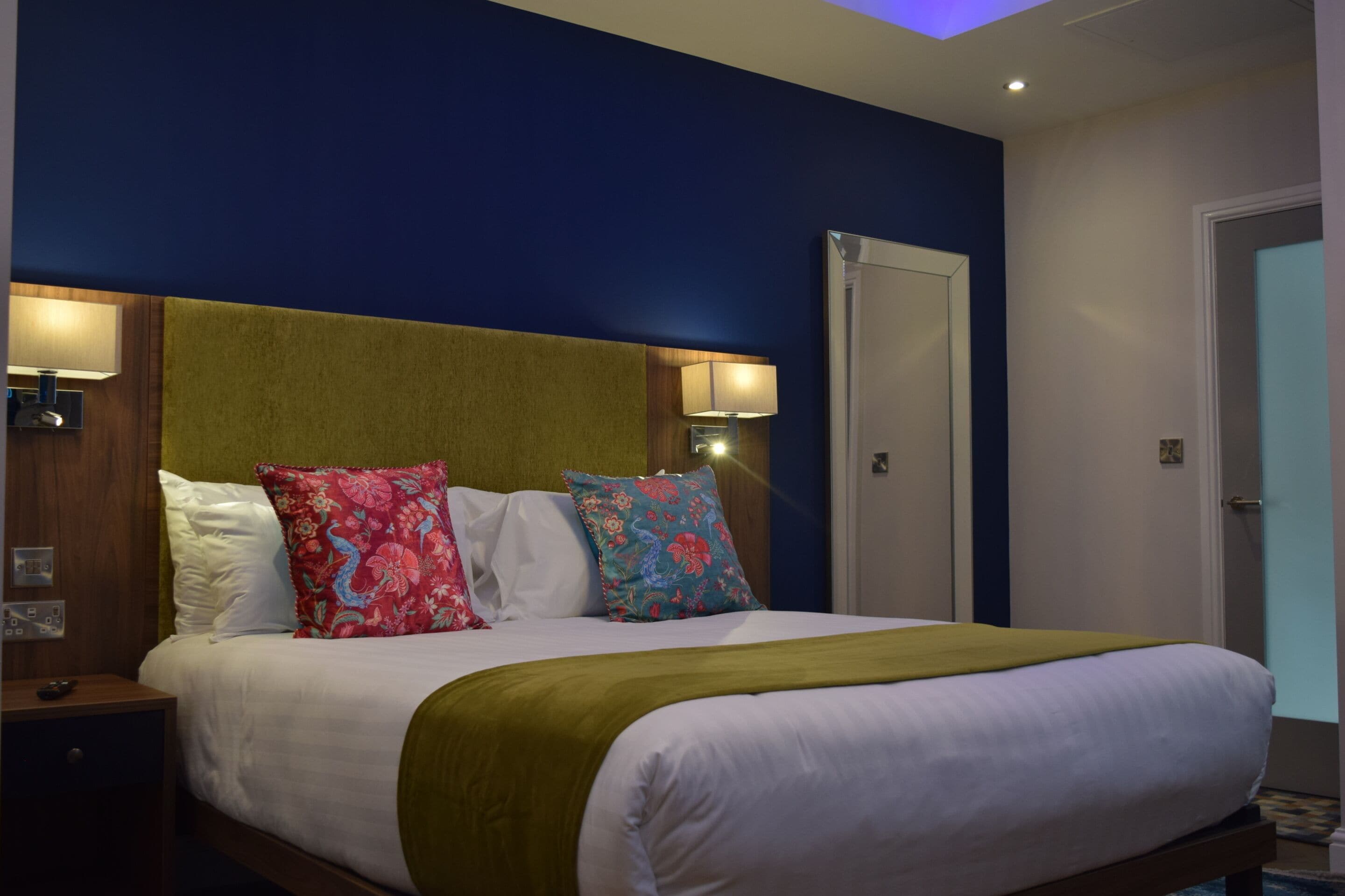 A hotel room with a bed, a nightstand, a lamp, and a door.