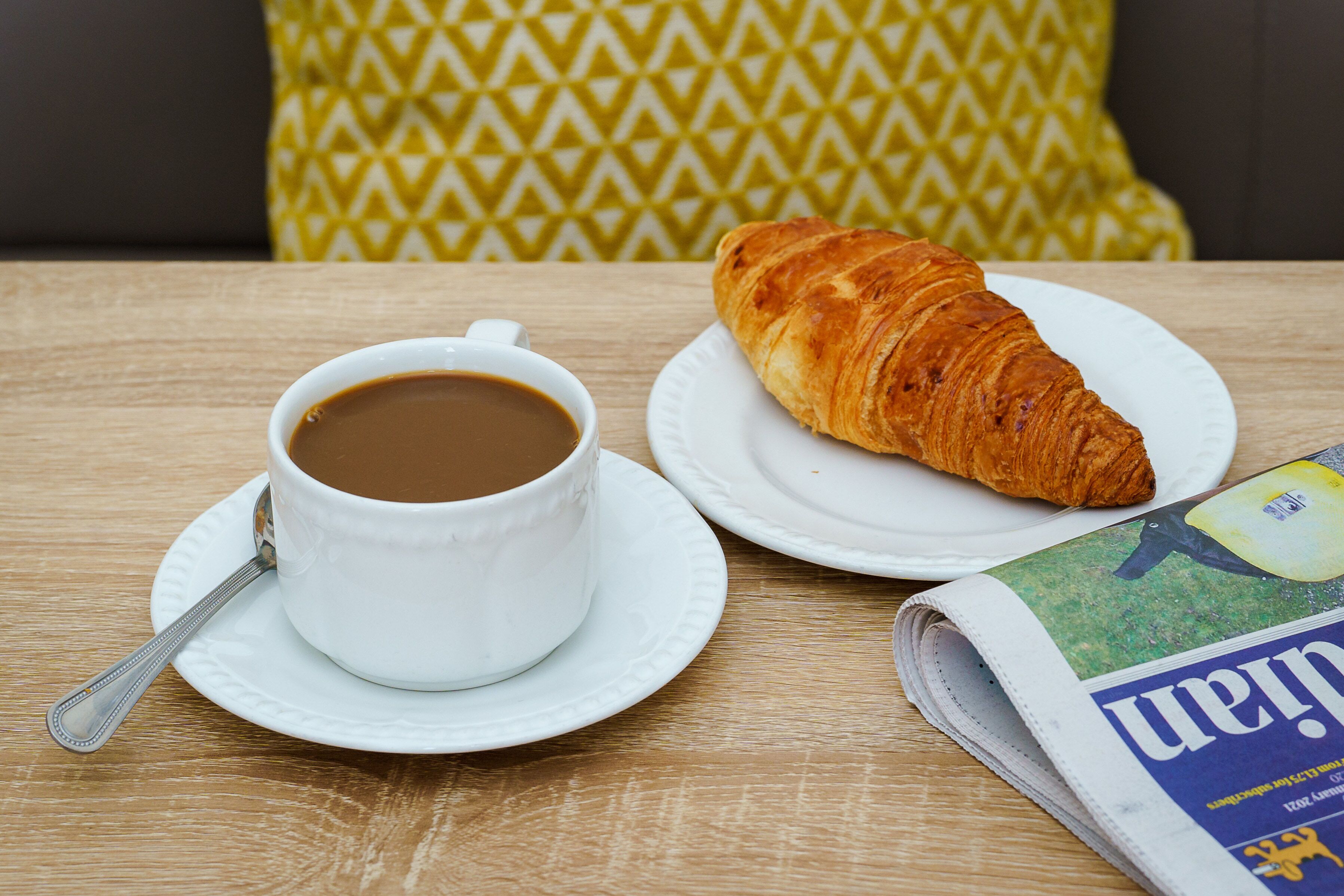 Una mesa con una taza de café, un croissant y un periódico.