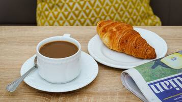 Una mesa con una taza de café, un croissant y un periódico.
