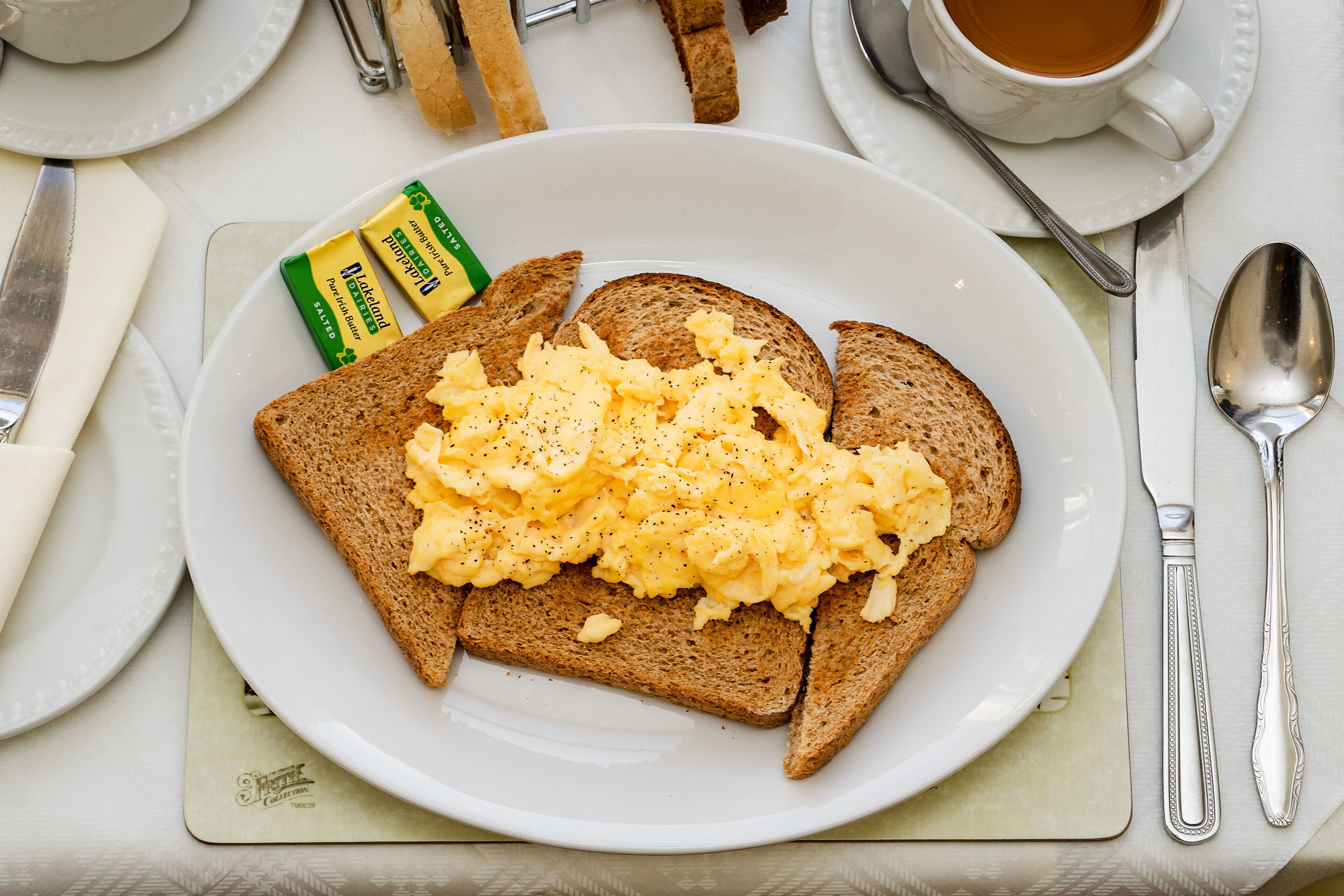 Un plato con huevos revueltos sobre tostadas, mantequilla y un bagel de semillas de amapola.